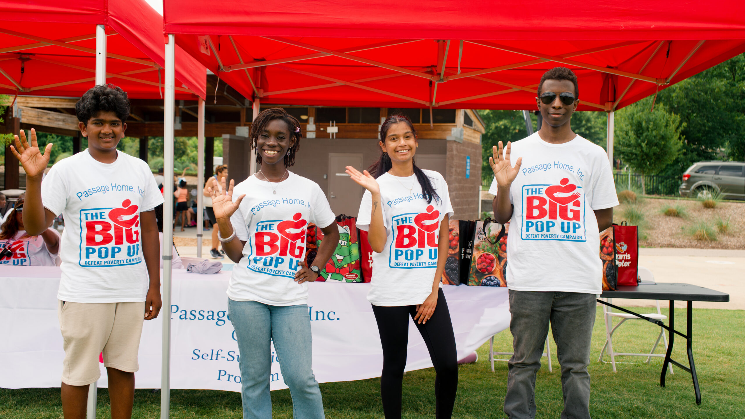 Four Passage Home volunteers waving at a community event
